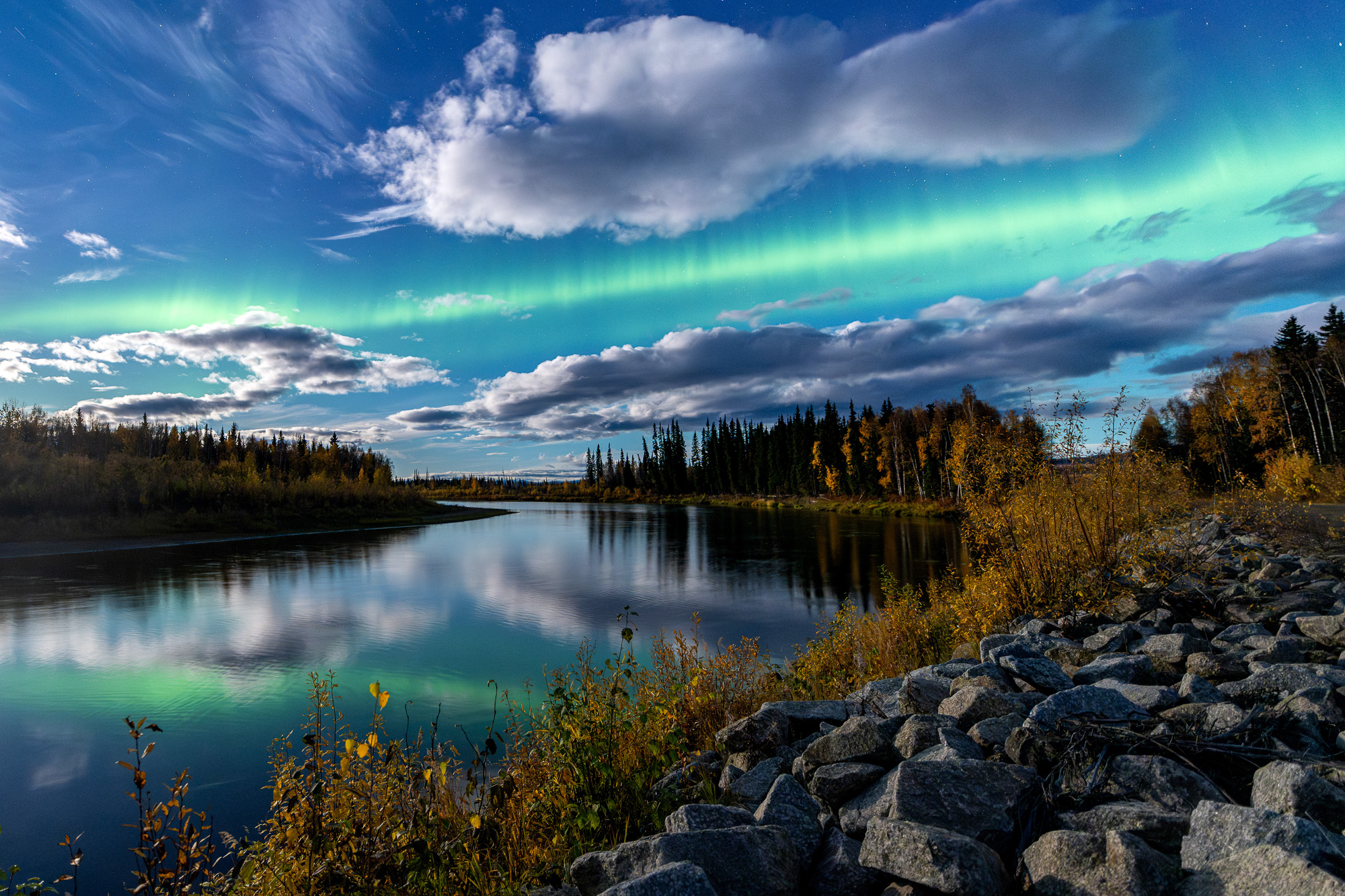 Aurora reflecting on a river under moonlight with fall colors in Alaska