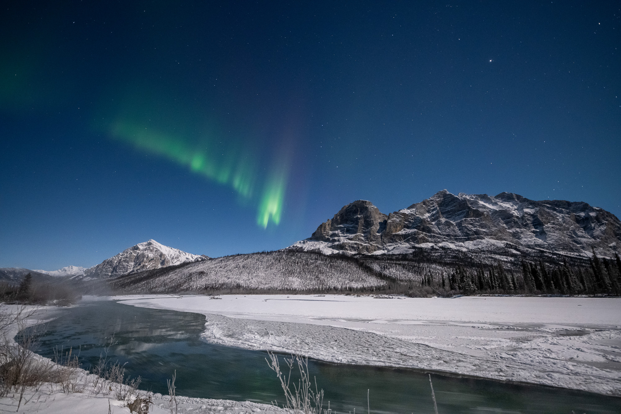 Aurora over a river with Sukakpak Mountain on a snowy moonlit night in Alaska